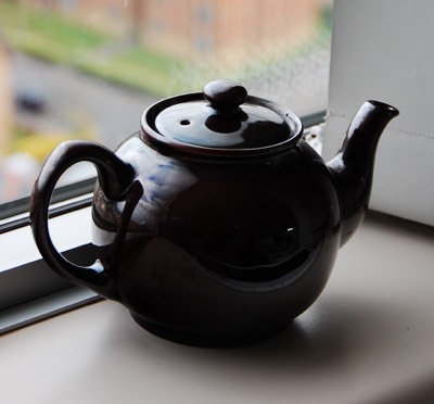 a black teapot placed on a shelf just inside a window